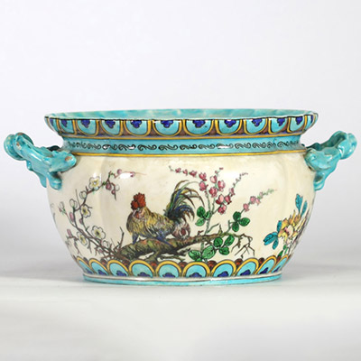 Théodore Deck (1823–1891) Importante jardinière en faïence émaillée, à décor polychrome d’inspiration extrême-orientale représentant un coq, des oiseaux, des papillons et des branchages fleuris en léger relief, sur fond crème. Frise supérieure ornée de motifs géométriques bleus et or. Ansés latérales en forme de dragons stylisés émaillés turquoise.