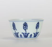 Chine, petit bol en porcelaine bleu et blanc à décor extérieur de caractères bouddhiques stylisés alternant avec des lotus, l’intérieur orné d’une fleur centrale, marque apocryphe à six caractères de 