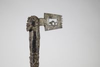 Hache cérémonielle en bronze à riche décor animalier – Afrique, probablement Congo, XXe siècle Hache cérémonielle coulée en bronze à patine foncée, ornée d’un décor finement ciselé figurant une tête anthropomorphe au sommet du manche, et une lame en forme de tranchant rectangulaire ajouré, décoré de motifs concentriques. Le fût présente une remarquable composition en relief représentant une faune