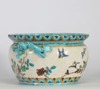 Théodore Deck (1823–1891) Importante jardinière en faïence émaillée, à décor polychrome d’inspiration extrême-orientale représentant un coq, des oiseaux, des papillons et des branchages fleuris en léger relief, sur fond crème. Frise supérieure ornée de motifs géométriques bleus et or. Ansés latérales en forme de dragons stylisés émaillés turquoise.