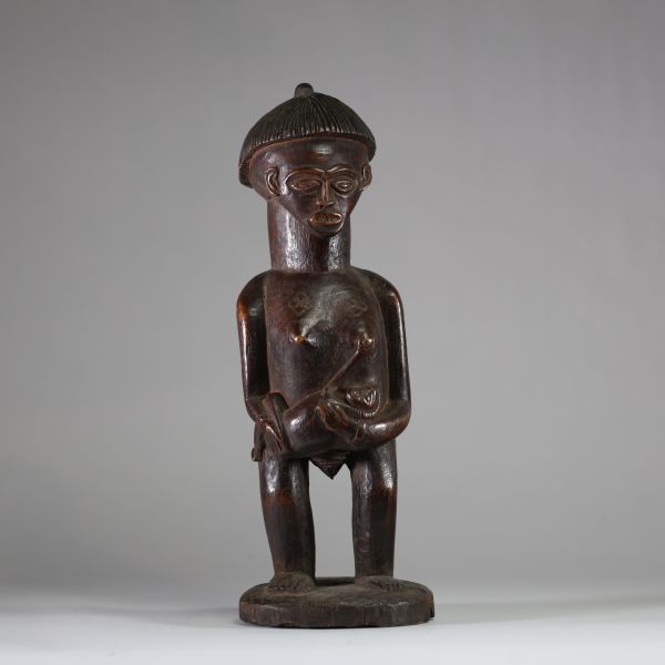 Statue de maternité, Lunda-Chokwe, zone frontière sud-est RDC / nord Angola. Bois sculpté, belle patine ancienne brune avec traces d’usage rituel, coiffe striée en casque avec crête, scarifications en losange et en chevrons, l'enfant saisissant activement le sein de sa mère. Cette statue constitue un témoignage remarquable d’un art de frontière entre les traditions Lunda, Chokwe et Luena, mêlant n