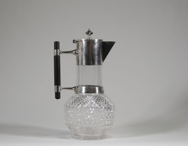 Christopher Dresser (1834–1904), Royaume-Uni Verseuse en verre et métal argenté Hukin & Heath, Birmingham, Angleterre, vers 1880  Cette verseuse élégante en verre soufflé et métal argenté, dotée d’un manche en ébène, est une création emblématique du célèbre designer britannique Christopher Dresser, figure pionnière du design industriel. Fabriquée par la maison Hukin & Heath vers 1880, elle illustr
