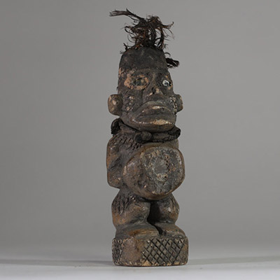 Ancienne figure rituelle en pierre  Bakongo, RD Congo. Travail de sculpture très fin. Le personnage a les mains posées sur le bilogo, protégé par un morceau de miroir. Le sommet du crâne est creusé et contient des plumes anciennes, renforçant sa dimension rituelle. Les jambes, le dos et les joues présentent des motifs gravés en croisillons, typiques de l'art Yombe. Un cordon textile est encore vis