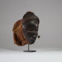 Ancien masque tribal avec coiffe « Mwana pwo » Chokwe/ Tshokwe, RD Congo, Angola. Bois. Très bel exemplaire bien conforme avec les yeux mi clos en « amande », le nez fin et allongé, la bouche entre-ouverte avec des dents « limées ». La coiffe ( samunganda) en raphia est élaborée et symbolise la coiffure des femmes de haut rang.  La patine est profondeet typique des masques ayant été frottés avec d