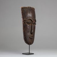Masque facial anthropomorphe Lele ( bashilele), RD Congo, région du Kasaï. Bois présentant une surface patinée ancienne, plus brillante et lisse dans les zones exposées. Trous sur les bords permettant l’attache d’ornements ou a une structure. Yeux sculptés en amande avec fente étroite. La bouche est petite et sculptée en légère saillie. Le nez est droit et allongé avec une base marquée. Exemplaire
