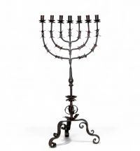 Grande menorah à sept branches en fer forgé, travail juif, vers 1900  Élégante et imposante menorah à sept branches en fer forgé, réalisée par un artisanat juif du début du XXe siècle. La structure finement travaillée, à décor de feuilles stylisées et de volutes, repose sur un piétement tripode à motif végétal. Ce chandelier, emblématique de la tradition rituelle juive