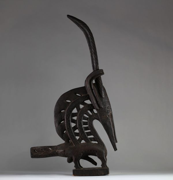 Ancien cimier « Chi Wara », Bamana, Mali. Bois. Il s’inscrit dans le style dit « horizontal du Sud », typique des régions de Sikasso et Bougouni. Ce style se distingue par des formes allongées, une représentation semi-abstraite, et une grande attention portée aux motifs incisés. Les éléments identifiables (cornes spiralées, oreilles recourbées, scarifications nombreuses, sexe proéminent ) sont car