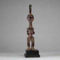 Statuette Bena Lulua, Région du Kasaï RD Congo. Bois. Très belle représentation d’ une figure féminine debout, aux proportions allongées. Tête légèrement surdimensionnée, ornée d'une coiffe cérémonielle monumentale se terminant en crosse verticale. Le visage montre des traits stylisés : yeux en amande, lèvres pleines, nez droit, et scarifications typiques sur le front, les joues et le menton. Le c