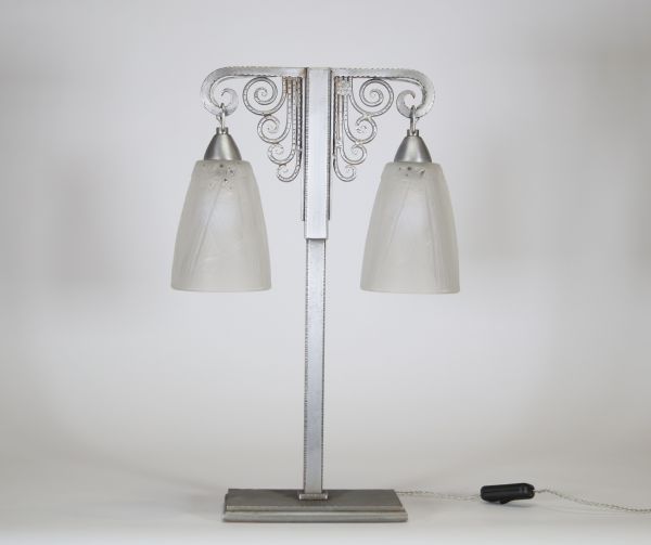 J. Vandôme & Muller Frères Lunéville, vers 1930 Lampe Art Déco à deux lumières en métal martelé nickelé et verrerie signée.  Structure en potence à deux bras terminés par d’élégantes volutes martelées, surmontant un fût vertical en métal à décor rayonnant. La base rectangulaire est signée J. Vandôme, artisan ou maison d’édition réputée pour ses œuvres de ferronnerie décorative dans les années 1930