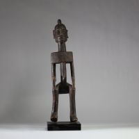 Statue masculine Dogon, Mali . Bois dense. Le style général est typique des productions Dogon anciennes, en particulier celles issues du plateau de Bandiagara. Le traitement géométrique du torse, l’élongation du cou, la posture figée et l’expression sobre indiquent une représentation d’ancêtre ou de figure spirituelle. La coiffe sagittale évoque les attributs cérémoniels du Hogon. La patine est an