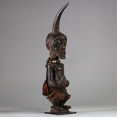 Fétiche Songye Nkisi, sous style Kalebwe, RD Congo. H : 46 cm. Figure masculine en bois, surmonté d’une corne rituelle, visage orné de clous de tapissier à fonction magique. Patine ancienne noire /brune, accessoires rituels suspendus (perles, fibres, cordelettes), cavités sous les bras. Nkisi de protection ou de justice activé par un « Nganga ». Style expressif et puissant propre aux Songye Kalebw