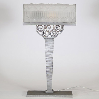 France, vers 1930 Lampe de bureau Art Déco en métal martelé nickelé et verre pressé à décor floral et géométrique.  Reposant sur une base rectangulaire, cette lampe présente un fût élancé à surface martelée, d’une sobriété élégante, souligné d’une finition nickelée mate. L’ensemble est rehaussé d’un nœud ornemental de volutes forgées à la main, typique du vocabulaire décoratif de l’époque.  L’abat