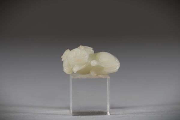 Chine - Sculpture en jade blanc représentant un chien chinois, fin de la dynastie Qing Sculpture délicatement taillée dans un jade blanc de belle qualité, figurant un chien chinois couché, le corps ramassé et la tête tournée vers l’avant. Le jade présente une teinte douce et homogène, typique des œuvres réalisées à la fin de la dynastie Qing. Le sujet animalier, fréquent dans l’art chinois, symbol