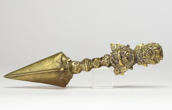Poignard rituel bouddhique, dit phurba, en bronze doré, à triple lame triangulaire. Le manche est orné d’un nœud symbolique à facettes et se termine par une représentation expressive de Vajrakilaya. Travail tibétain, XIXe siècle.