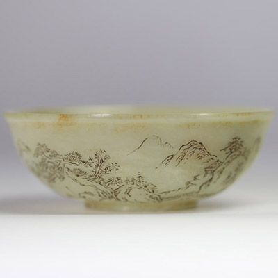 Bol en jade céladon finement gravé d’un paysage montagneux et d’un poème calligraphié, marqué Qianlong  Bol circulaire en jade de teinte céladon très pâle, finement incisé d’un décor continu représent