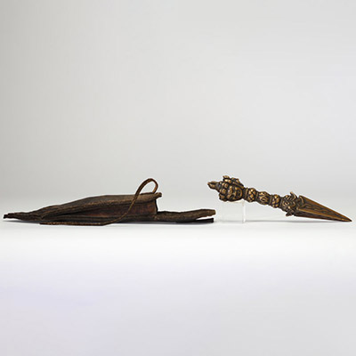 Rare phurba tibétain avec son fourreau, triple lame triangulaire et décoré à la poignée d’une tête de divinité courroucée finement ciselée son fourreau d’origine en cuir gravé, de forme effilée, avec son cordon de suspension, élément rare pour ce type d’objet. probablement XVIIIe siècle