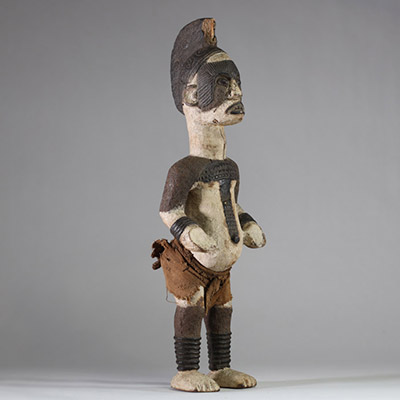 Statue Igbo « Alusi ». Nigéria. Bois, textile. Représentation masculine de type Alusi, divinité secondaire ou esprit tutélaire propre au peuple Igbo (sud-est du Nigeria), vénérée dans des sanctuaires collectifs ou familiaux. Grande crête sagittale sculptée d’une coiffe en éventail semi circulaire, ornée de motifs en spirales. Front bombé, yeux globuleux en amande, sans pupille, sourcils et joues m