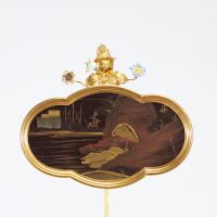 Bougeoir à écran, en bronze ciselé et doré, à décor ajouré de rinceaux feuillagés ponctués de fleurs en porcelaine polychrome de style Meissen. L’ensemble est surmonté d’un écran en laque du Japon de forme chantournée, à décor de paysage lacustre doré dans le goût des exportations de l’époque Meiji. Travail pouvant être attribué à la prestigieuse maison parisienne de l’Escalier de Cristal, vers 18