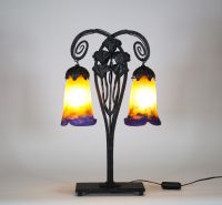 Muller Frères, Lunéville, vers 1905 Lampe à deux lumières en fer forgé martelé à décor de ginkgo biloba et verreries multicouches signées.  Superbe lampe Art Nouveau en fer forgé patiné noir, montée sur une base rectangulaire, s’élevant en double col de cygne à volutes stylisées. Le fût est orné de feuilles et hampes florales de ginkgo biloba, motif emblématique du symbolisme végétal de la Belle É