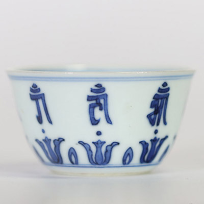 Chine, petit bol en porcelaine bleu et blanc à décor extérieur de caractères bouddhiques stylisés alternant avec des lotus, l’intérieur orné d’une fleur centrale, marque apocryphe à six caractères de 