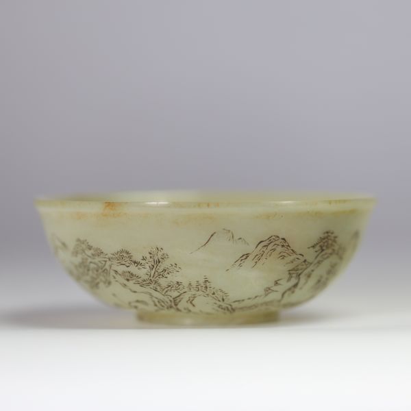 Bol en jade céladon finement gravé d’un paysage montagneux et d’un poème calligraphié, marqué Qianlong  Bol circulaire en jade de teinte céladon très pâle, finement incisé d’un décor continu représent