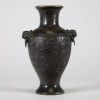Vase en bronze à décor archaïsant et anses en têtes de lion, Chine Élégant vase en bronze de forme balustre, reposant sur un pied évasé et doté d’un col évasé à bord légèrement ourlé. Le corps est entièrement orné en léger relief d’un décor sinueux de rinceaux et volutes évoquant les motifs archaïques de la période des Royaumes Combattants ou des bronzes rituels Shang-Zho