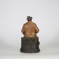 Bernard Bloch (atelier BB), Bohême, fin XIXe – début XXe siècle Pot à tabac en terre cuite polychrome figurant un homme assoupi vêtu d’un costume campagnard, assis sur une souche, les yeux mi-clos, un journal déployé sur les genoux.