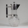 Christopher Dresser (1834–1904), Royaume-Uni Verseuse en verre et métal argenté Hukin & Heath, Birmingham, Angleterre, vers 1880  Cette verseuse élégante en verre soufflé et métal argenté, dotée d’un manche en ébène, est une création emblématique du célèbre designer britannique Christopher Dresser, figure pionnière du design industriel. Fabriquée par la maison Hukin & Heath vers 1880, elle illustr