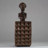 Plateau de jeu type « awalé » rituel Songye, RD Congo. Bois ancien, figure anthropomorphe stylisée, dont la partie inférieure est un plateau creusé de 24 alvéoles disposées en quatre rangées de six. Le personnage reprend les canons classiques de la culture Songye avec les bras collés au corps, et un ventre proéminent. Bel objet initiatique et symbolique à la croisée du ludique et du sacral, associ