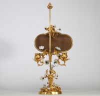 Bougeoir à écran, en bronze ciselé et doré, à décor ajouré de rinceaux feuillagés ponctués de fleurs en porcelaine polychrome de style Meissen. L’ensemble est surmonté d’un écran en laque du Japon de forme chantournée, à décor de paysage lacustre doré dans le goût des exportations de l’époque Meiji. Travail pouvant être attribué à la prestigieuse maison parisienne de l’Escalier de Cristal, vers 18