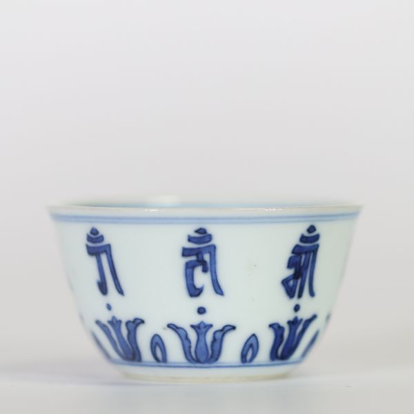 Chine, petit bol en porcelaine bleu et blanc à décor extérieur de caractères bouddhiques stylisés alternant avec des lotus, l’intérieur orné d’une fleur centrale, marque apocryphe à six caractères de 