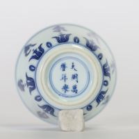 Chine, petit bol en porcelaine bleu et blanc à décor extérieur de caractères bouddhiques stylisés alternant avec des lotus, l’intérieur orné d’une fleur centrale, marque apocryphe à six caractères de 