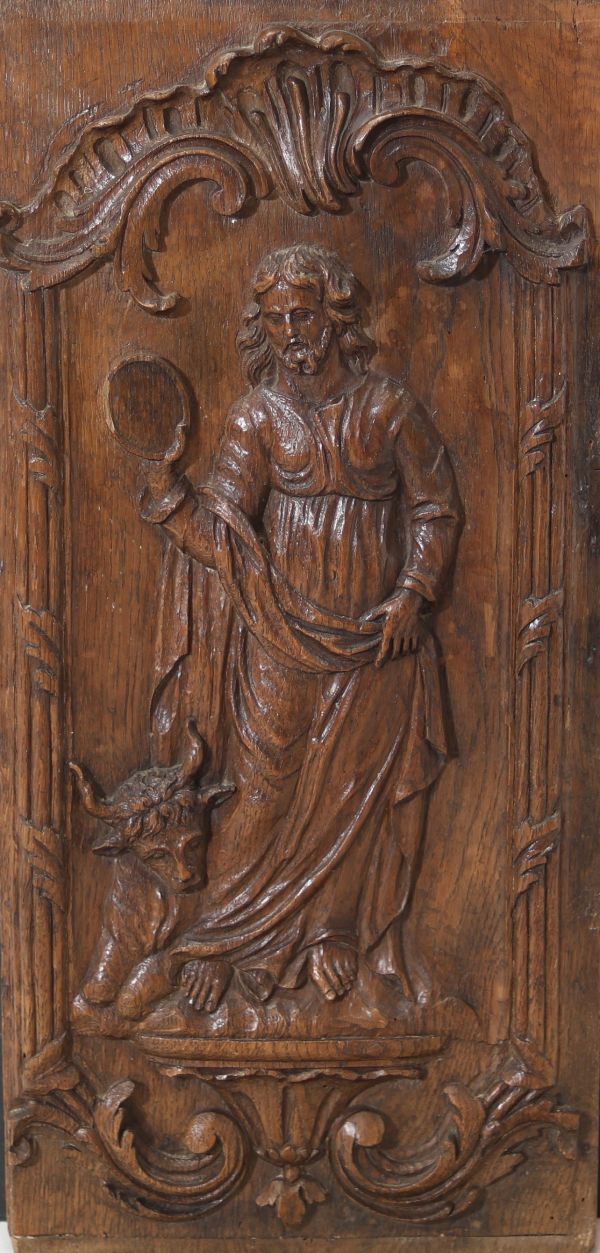 Panneau en chêne finement sculpté en haut relief, figurant saint Luc. L’évangéliste est représenté debout, en tunique et manteau, tenant dans sa main droite un objet circulaire. L’ensemble est encadré d’un riche décor rocaille à enroulements feuillagés et coquille.Travail régional, probablement d’Europe du Sud ou de l’Est, d’époque XVIIIe siècle.