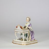 Figurine en porcelaine polychrome de la manufacture de Meissen « Jeune femme devant un petit piano ou clavecin. La base à décor moulé de lambrequins dorés repose sur un socle rectangulaire. Marque aux