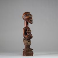 Fétiche rituel figurant un nkishi protecteur ethnie Songye, sous groupe Kalebwe. Figure dotée d'un long cou, de pieds larges, d'un visage souriant et d'une ceinture abdominale contenant une charge organique et présentant autrefois une corne magique au sommet du crâne. Usure rituelle et patine ancienne authentifient son usage. Très belle représentation Kalebwe, entre force symbolique et expressivit