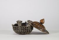 Kapala rituel, Tibet, XVIIIᵉ–XIXᵉ siècle Récipient rituel tibétain de type kapala, composé d’un corps en argent richement décoré de frises de têtes de kirtimukha, de chaînes perlées et de motifs stylisés. Le couvercle est en cuivre martelé, à décor gravé de pétales de lotus rayonnants, surmonté d’un prend finial en forme de flamme, symbole de sagesse dans le bouddhisme tantrique. Aux extrémités, d