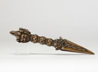 Rare phurba tibétain avec son fourreau, triple lame triangulaire et décoré à la poignée d’une tête de divinité courroucée finement ciselée son fourreau d’origine en cuir gravé, de forme effilée, avec son cordon de suspension, élément rare pour ce type d’objet. probablement XVIIIe siècle