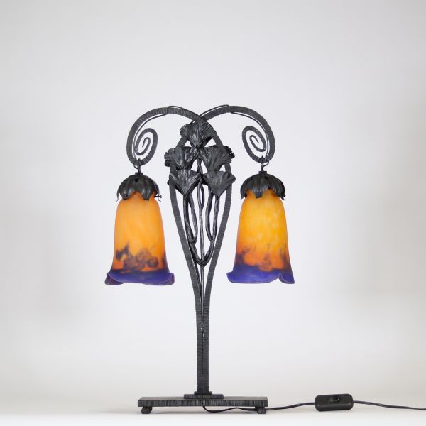 Muller Frères, Lunéville, vers 1905 Lampe à deux lumières en fer forgé martelé à décor de ginkgo biloba et verreries multicouches signées.  Superbe lampe Art Nouveau en fer forgé patiné noir, montée sur une base rectangulaire, s’élevant en double col de cygne à volutes stylisées. Le fût est orné de feuilles et hampes florales de ginkgo biloba, motif emblématique du symbolisme végétal de la Belle É