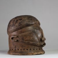 Masque-casque en bois, de forme hémisphérique Tabwa, RD congo. Visage sculpté avec un nez droit, saillant, de forme anguleuse, très caractéristique des styles Tabwa et Luba-Tabwa. Les yeux sont incrustés de cauris, Les scarifications faciales linéaires et parallèles, courant des tempes vers la bouche, sont typiques des traditions Tabwa. La patine naturelle, les abrasions autour de la base perforée
