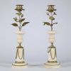 Paire de bougeoirs en marbre et bronze doré, travail de style Louis XVI Élégante paire de bougeoirs en marbre blanc veiné à base circulaire ornée de guirlandes en chaînette de bronze doré, la partie centrale prenant la forme d’un vase balustre, surmonté d’un décor végétal en bronze doré figurant une tige florale montée en candélabre, chaque fleur formant bobèche.  L’ensemble évoque avec fidélité l