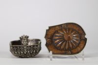 Kapala rituel, Tibet, XVIIIᵉ–XIXᵉ siècle Récipient rituel tibétain de type kapala, composé d’un corps en argent richement décoré de frises de têtes de kirtimukha, de chaînes perlées et de motifs stylisés. Le couvercle est en cuivre martelé, à décor gravé de pétales de lotus rayonnants, surmonté d’un prend finial en forme de flamme, symbole de sagesse dans le bouddhisme tantrique. Aux extrémités, d