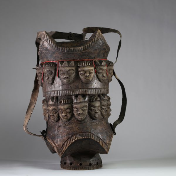 Très rare boîte rituelle de grande taille Pendé, RD Congo. Dotée d’un couvercle emboîtant d’une sangle en cuir permettant le transport. Elle est ornée de 24 visages humains stylisés en frise continue sur le pourtour bois. Des perles rouges sont fixées sur accentuant la dimension rituelle. Une fente ancienne est visible sur un bord, témoignant d’un usage prolongé et d’un vieillissement naturel du b