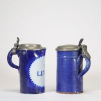 Lot de deux chopes en faïence émaillée de Bruxelles, à décor bleu cobalt et inscriptions « ½ LITRE » en réserve. Chaque pièce est coiffée d’un couvercle en étain fin XIXe – début XXe