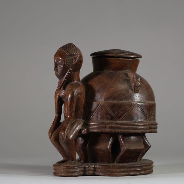 Oracle à souris ( bo num) Baoulé,  côte d’Ivoire. Bois dense, relativement ancien, à patine brune, représentant une figure masculine  assise, soutenant un récipient divinatoire circulaire finement décoré. Un trou circulaire obturé sous la base atteste de l’usage rituel de cette pièce, destinée aux pratiques divinatoires du devin (komien). Le style correspond à la statuaire Baoulé classique du cent