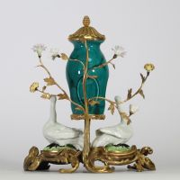 Fontaine à parfum, composée d’un vase en porcelaine de Chine émaillée bleu turquoise, datable du XVIIIe siècle, surmontée d’un couvercle orné d’une pomme de pin dorée. L’ensemble repose sur une base rocaille en bronze ciselé et doré, richement décorée de deux cygnes en porcelaine de Meissen, posés sur des tertres verts. Le décor est complété de fleurs en porcelaine polychrome, probablement de styl