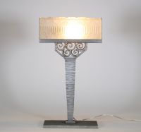 France, vers 1930 Lampe de bureau Art Déco en métal martelé nickelé et verre pressé à décor floral et géométrique.  Reposant sur une base rectangulaire, cette lampe présente un fût élancé à surface martelée, d’une sobriété élégante, souligné d’une finition nickelée mate. L’ensemble est rehaussé d’un nœud ornemental de volutes forgées à la main, typique du vocabulaire décoratif de l’époque.  L’abat