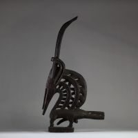 Ancien cimier « Chi Wara », Bamana, Mali. Bois. Il s’inscrit dans le style dit « horizontal du Sud », typique des régions de Sikasso et Bougouni. Ce style se distingue par des formes allongées, une représentation semi-abstraite, et une grande attention portée aux motifs incisés. Les éléments identifiables (cornes spiralées, oreilles recourbées, scarifications nombreuses, sexe proéminent ) sont car