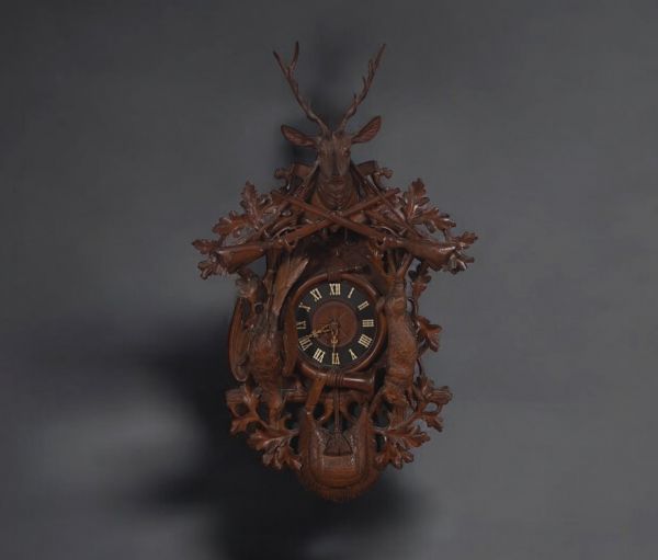 Large Black Forest ‘Cuckoo’ clock in carved wood decorated with hunting trophies, hare, partridge, stag's head and rifles.