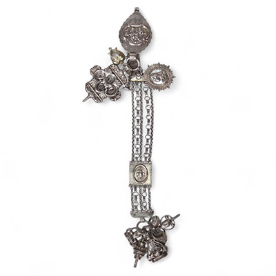 Chatelaine en argent, Pays-Bas, XIXᵉ siècle Chatelaine en argent composée de plusieurs éléments richement décorés, réunis par une double chaîne à maillons ciselés. L’ensemble est orné de médaillons à motifs en bas-relief, de pendentifs fonctionnels (grelots, sifflet, étui, petite théière ou vinaigrier...), et d’un fermoir principal gravé de scènes figuratives.  Le poinçon au lion marchant n°2, vis