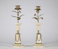 Paire de bougeoirs en marbre et bronze doré, travail de style Louis XVI Élégante paire de bougeoirs en marbre blanc veiné à base circulaire ornée de guirlandes en chaînette de bronze doré, la partie centrale prenant la forme d’un vase balustre, surmonté d’un décor végétal en bronze doré figurant une tige florale montée en candélabre, chaque fleur formant bobèche.  L’ensemble évoque avec fidélité l